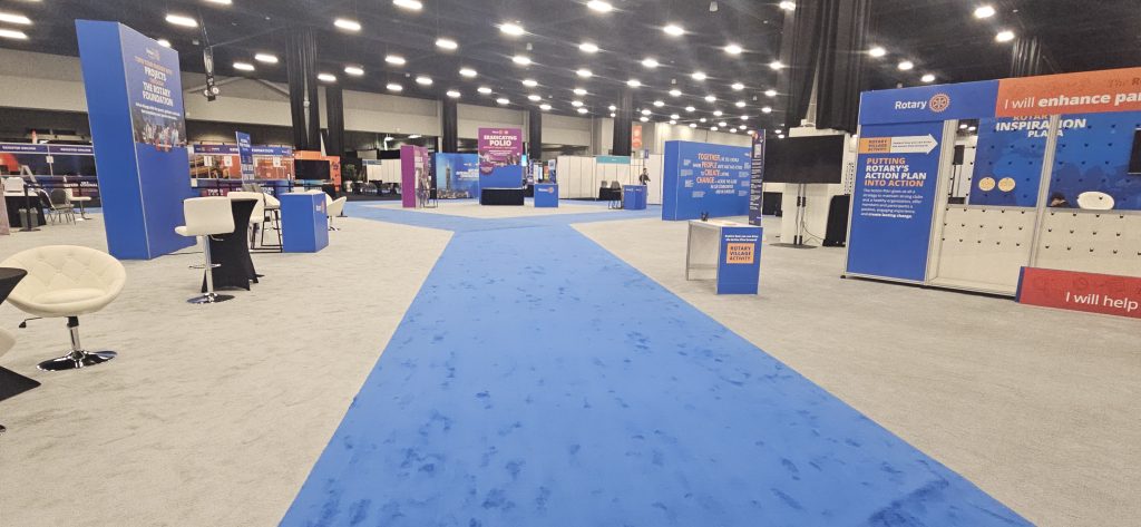 Wide view of the exhibition hall with blue carpet walkways and branded exhibit areas installed for the Rotary International Convention